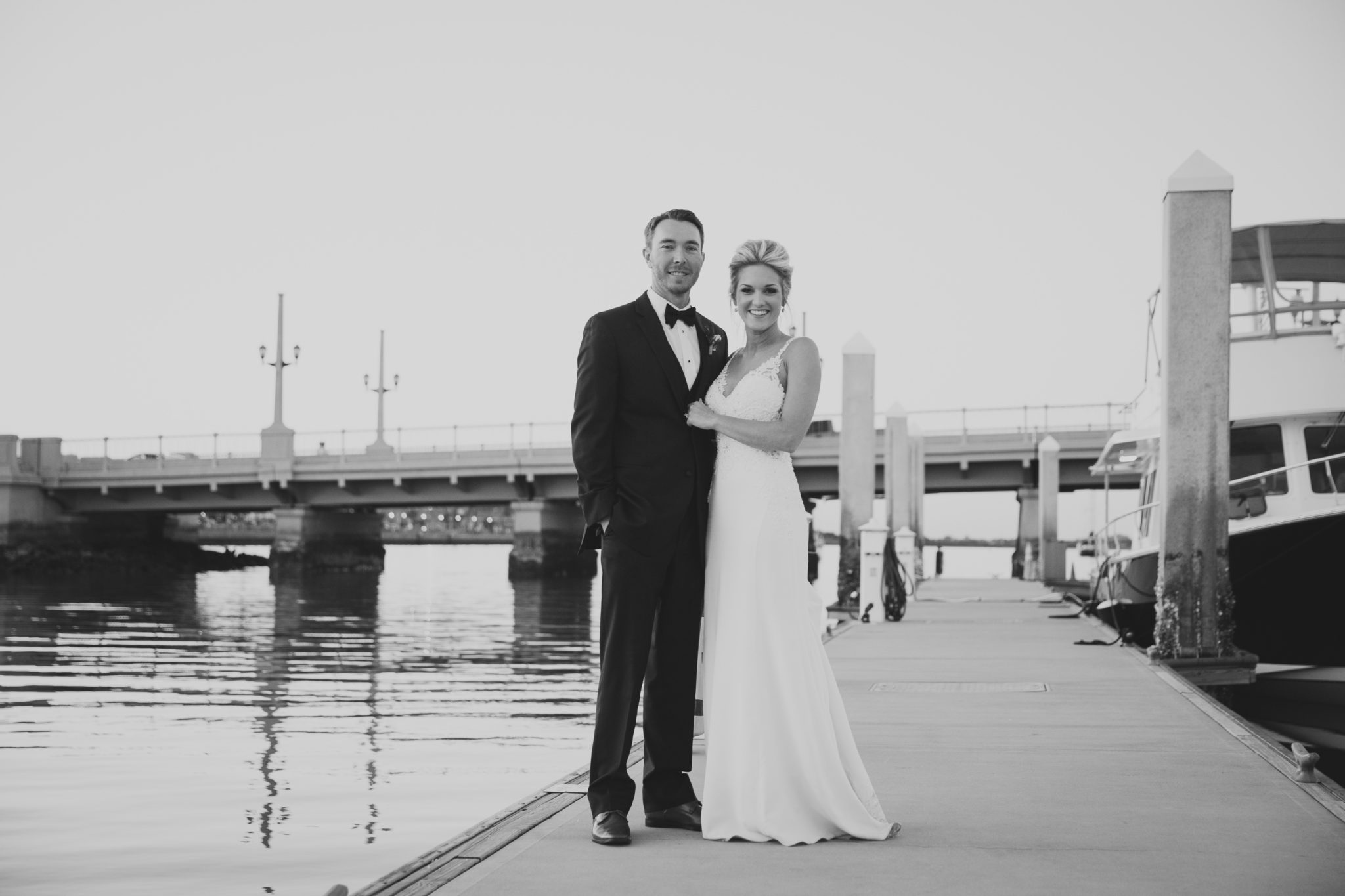bride and groom standing on dock in front of bridge