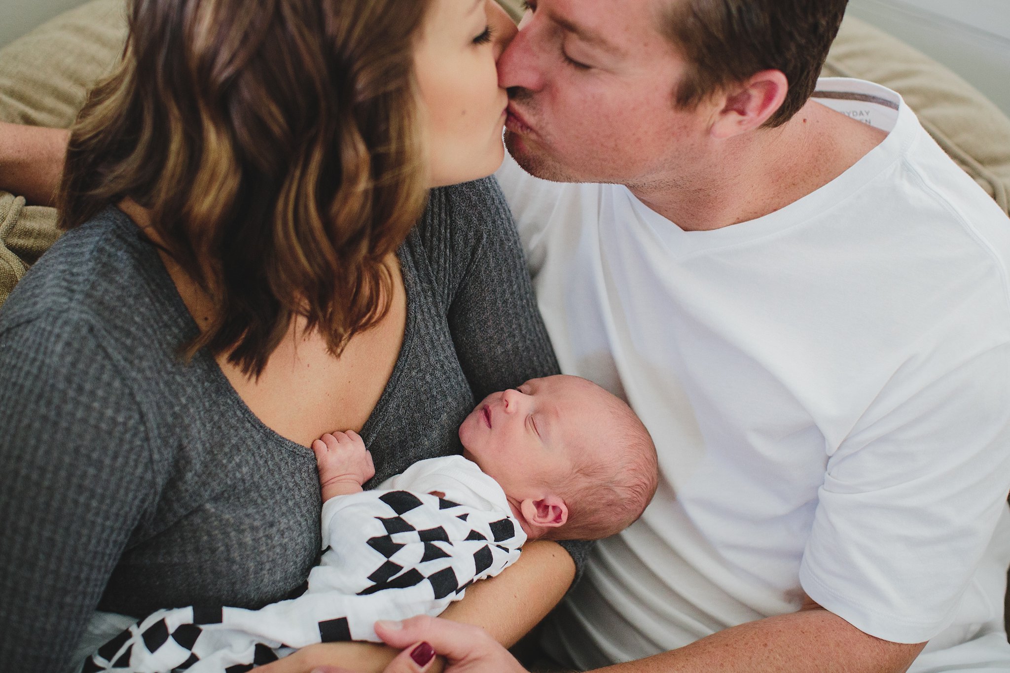 couple kissing while holding newborn baby