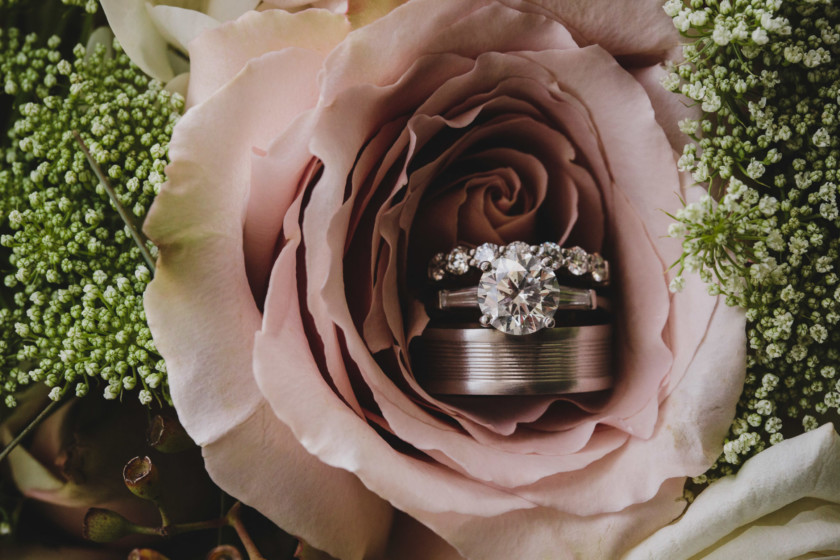 engagement ring and wedding bands arranged in dusty rose flower