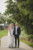 bride and groom holding hands, standing in pathway under trees