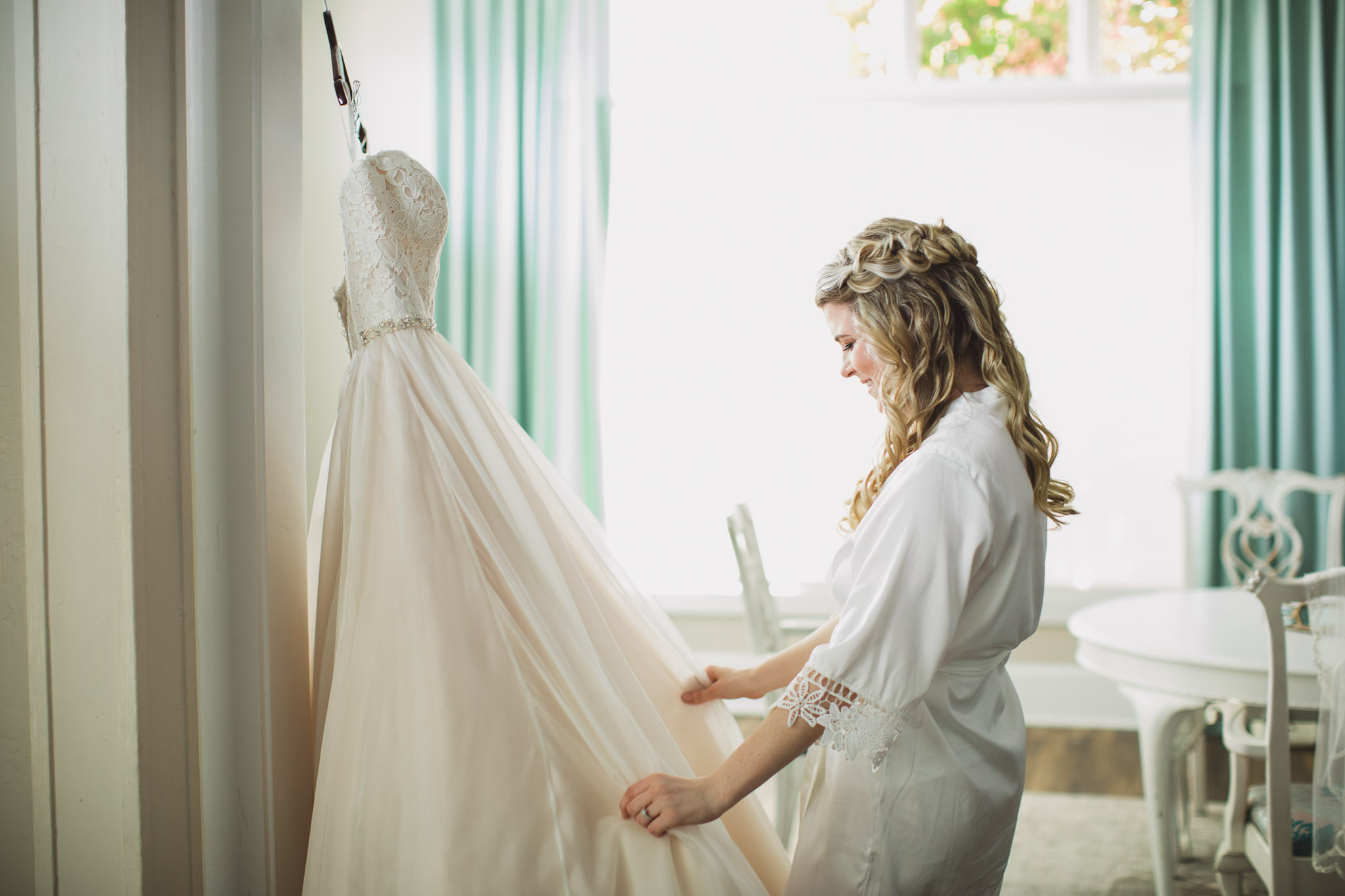 bride in bathrobe looking at her wedding gown in bridal suite at whit room