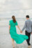 couple holding hands walking towards the beach with woman's dress flowing in the wind