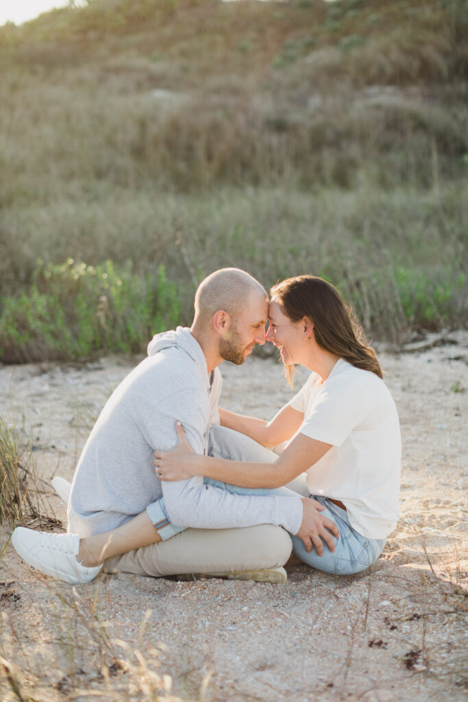 couple sitting on beach and facing each other during engagement photos