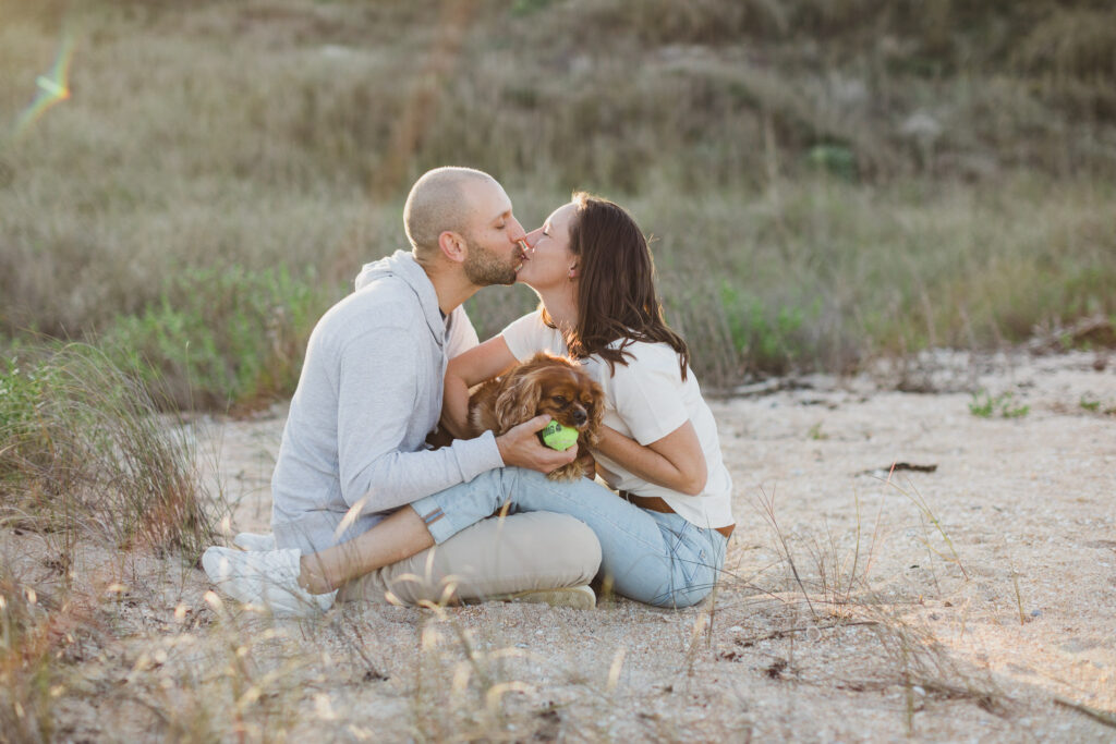 couple kissing and holding their dog on the beach