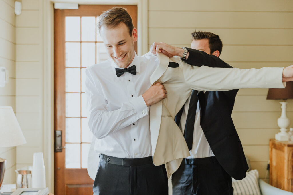 groom getting white suit jacket on with help from best man at oyster bay yacht club