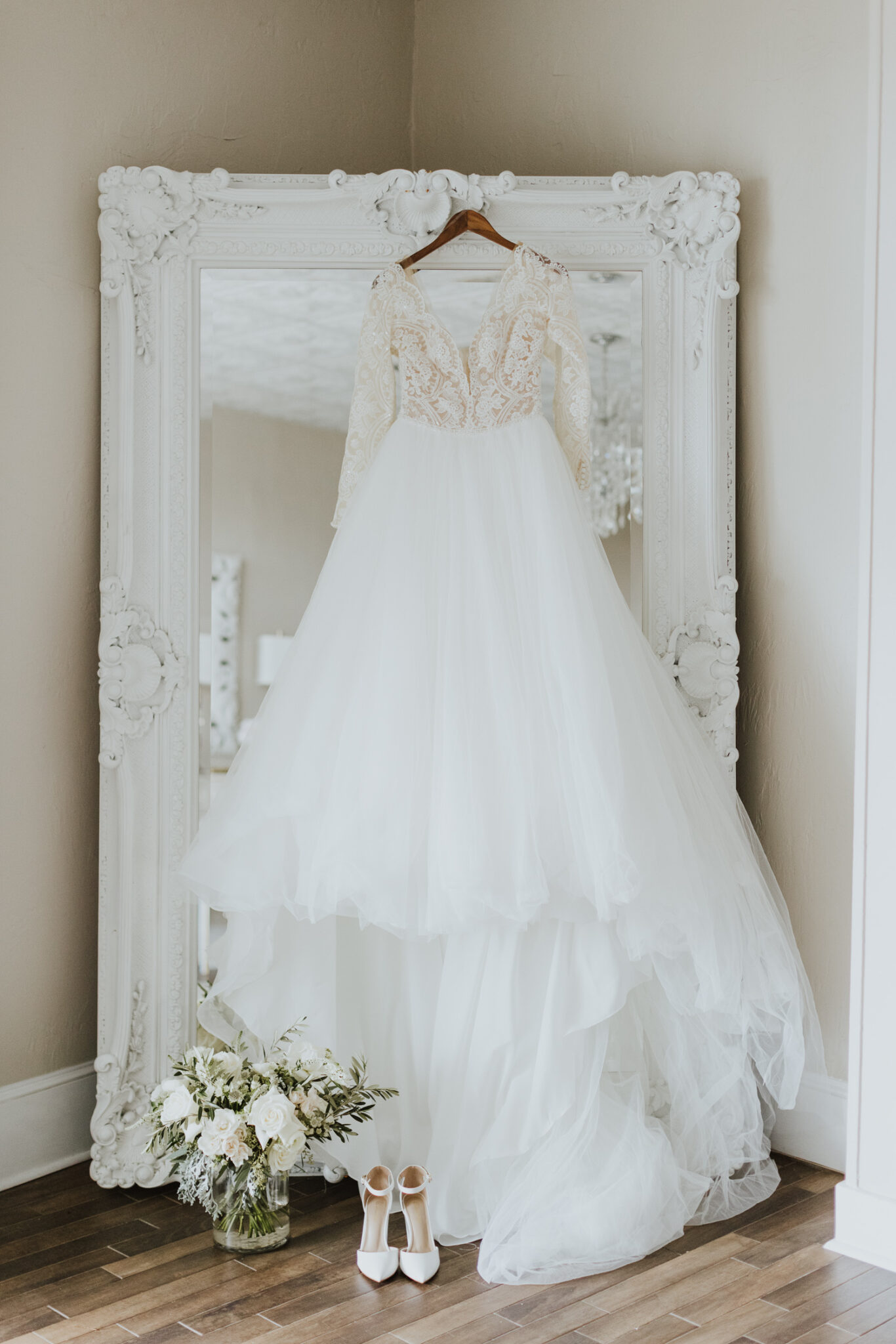 bridal gown hanging off large white mirror in white room bridal suite 