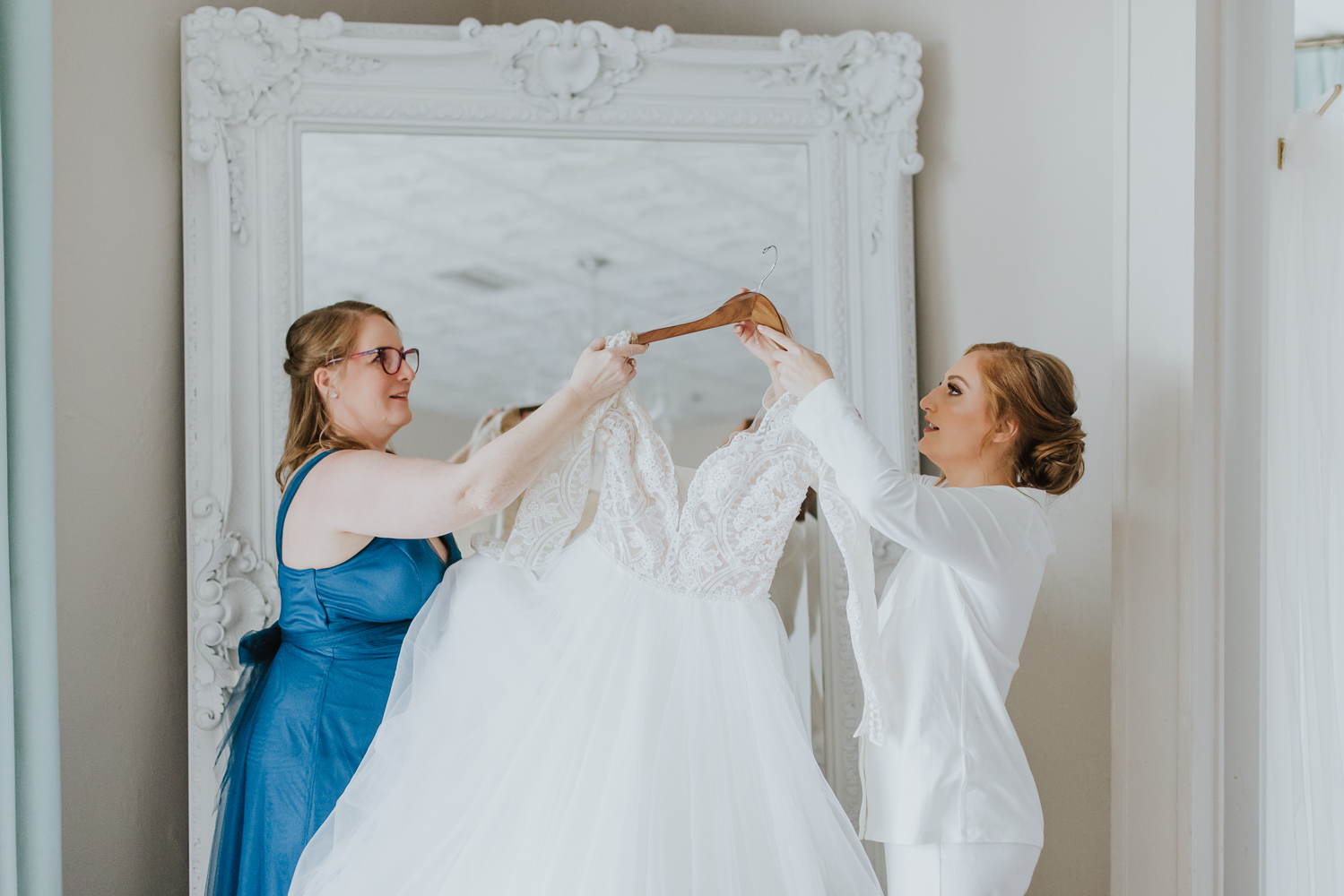 bride and her mom getting dress down to get changed in bridal suite of white room 