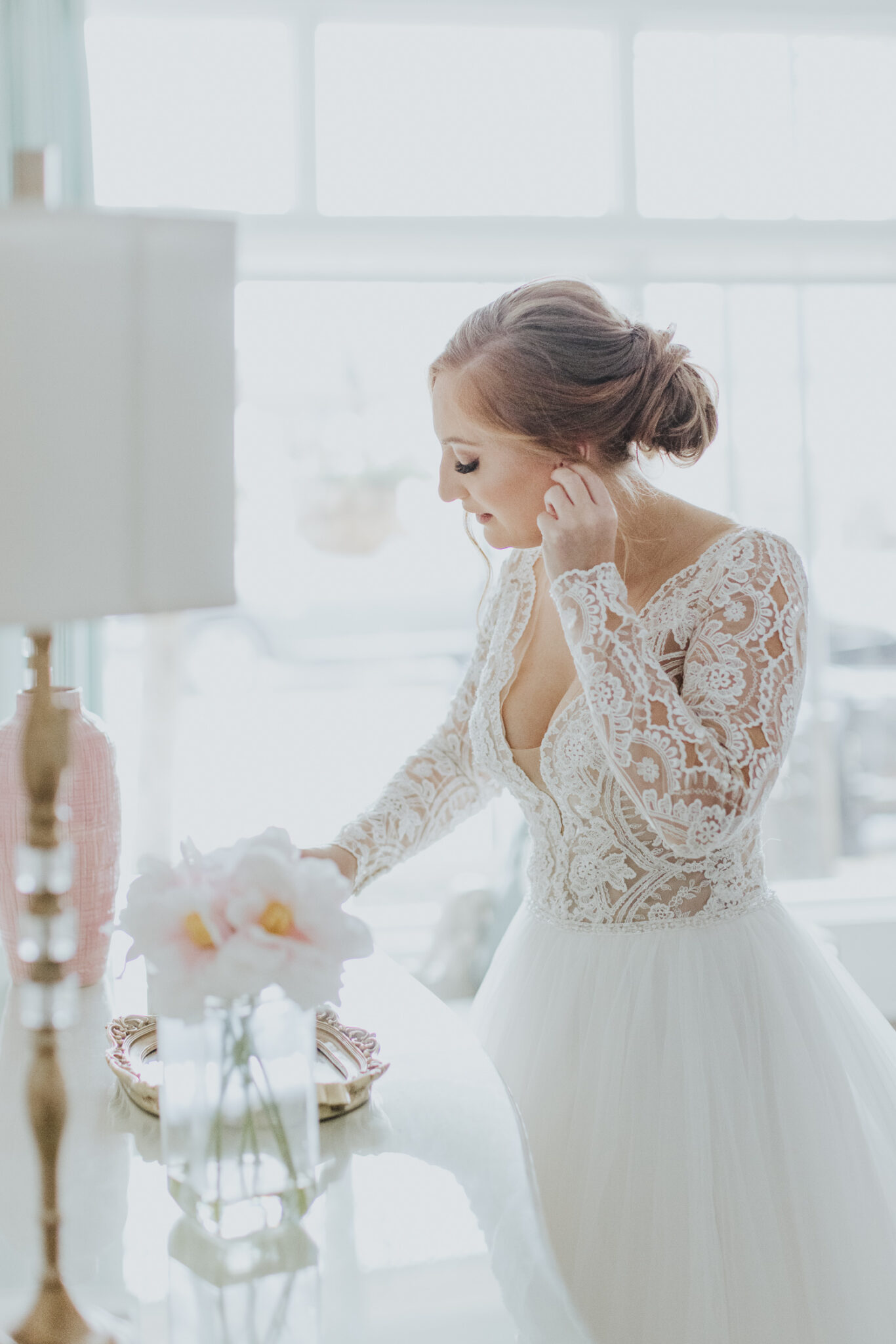 bride at mirror putting earrings on before white room wedding 
