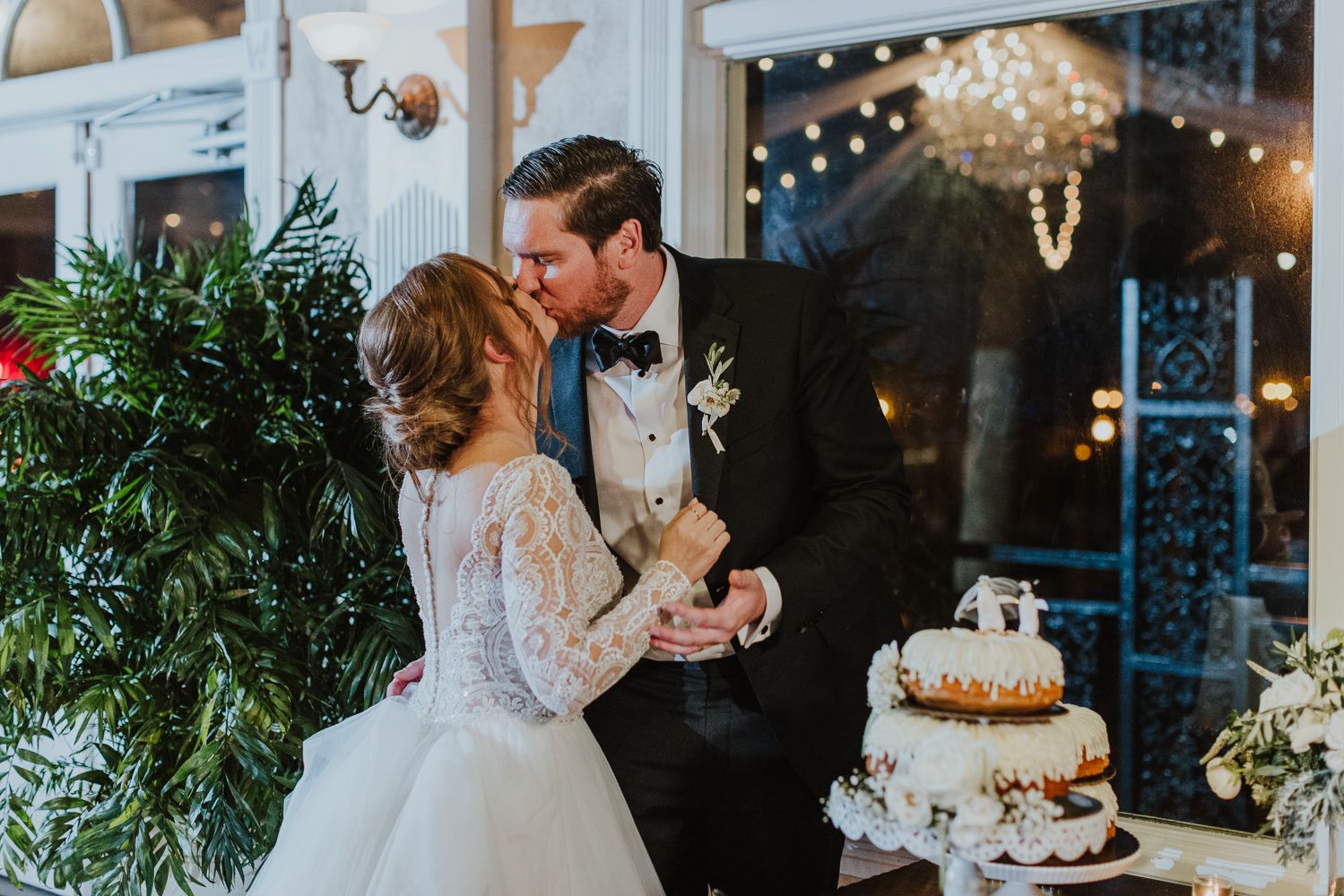 bride and groom kissing after cutting their cake at their white room wedding reception 