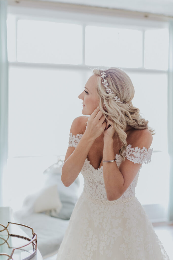 bride putting in earrings in front of window of white room grand ballroom bridal suite