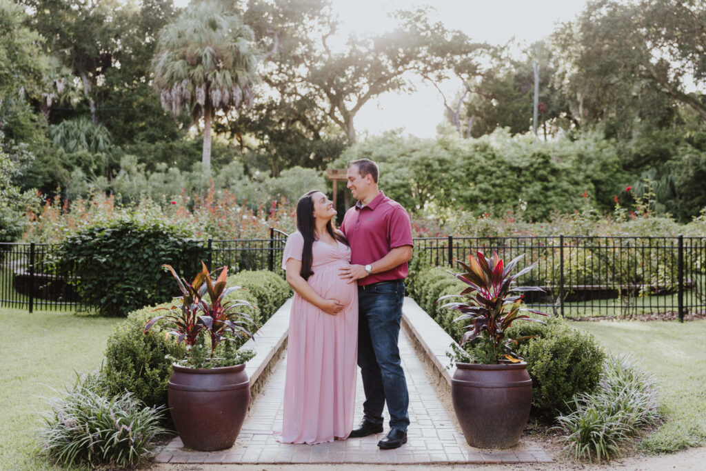 couple standing together in front of rose garden at washington oaks garden touching belly during maternity session 