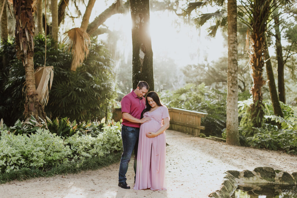 couple standing together in washington oaks garden touching and looking at belly during maternity session