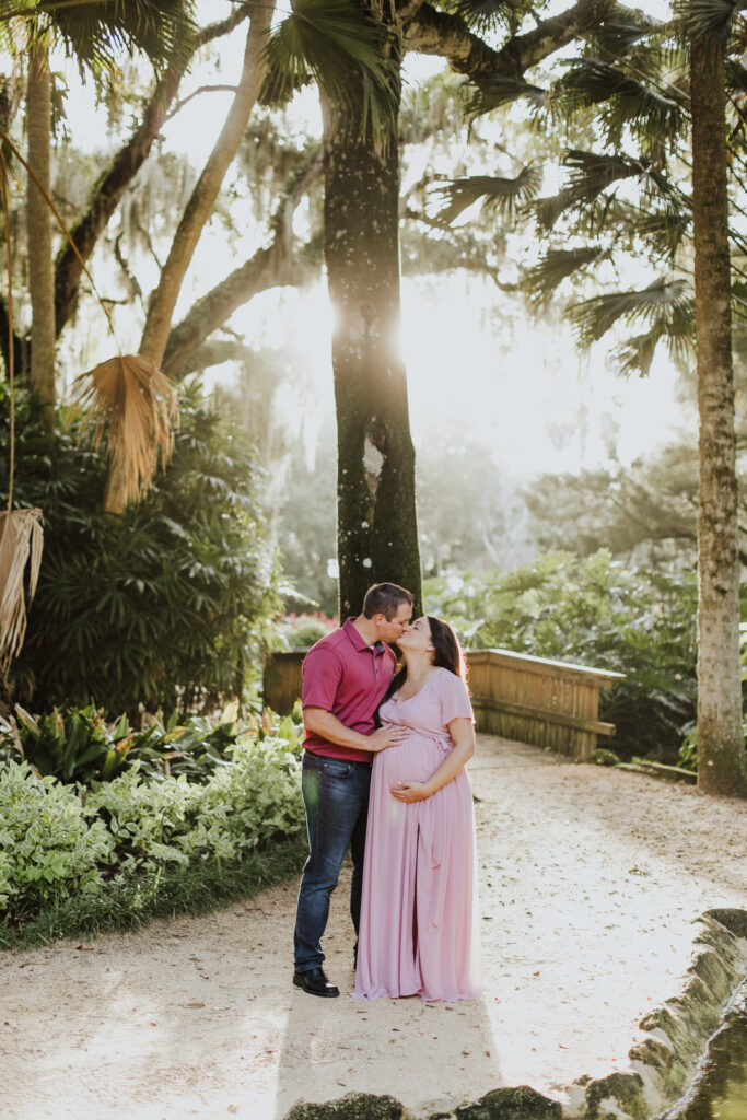 couple standing together and kissing while standing in path of washington oaks garden touching belly during maternity session
