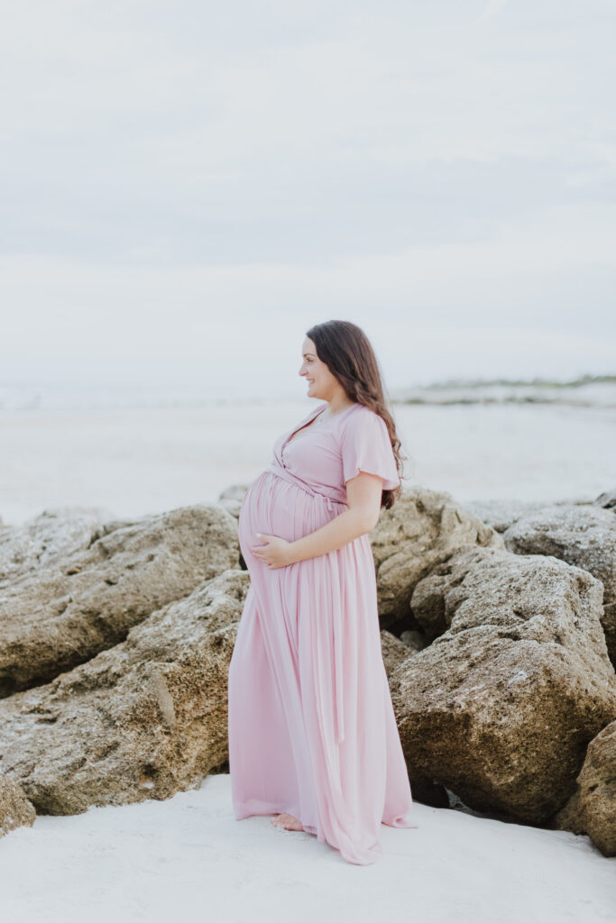 mom to be standing on beach at washington oaks looking out to the ocean during maternity session