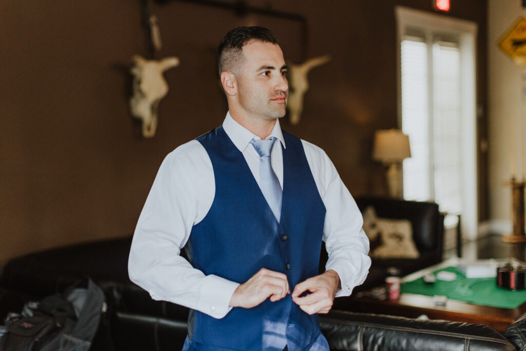 groom buttoning up vest on navy suit in the groom's suite of bowing oaks in jacksonville fl