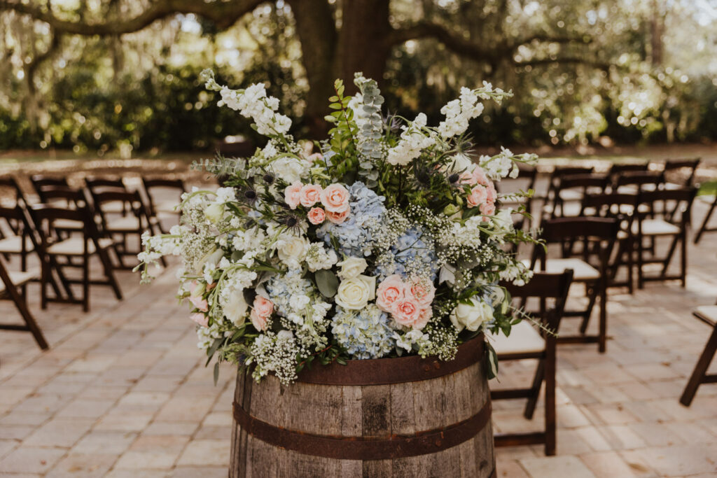 white, pink and light blue wedding floral arrangement on barrel at wedding ceremony area of bowing oaks 