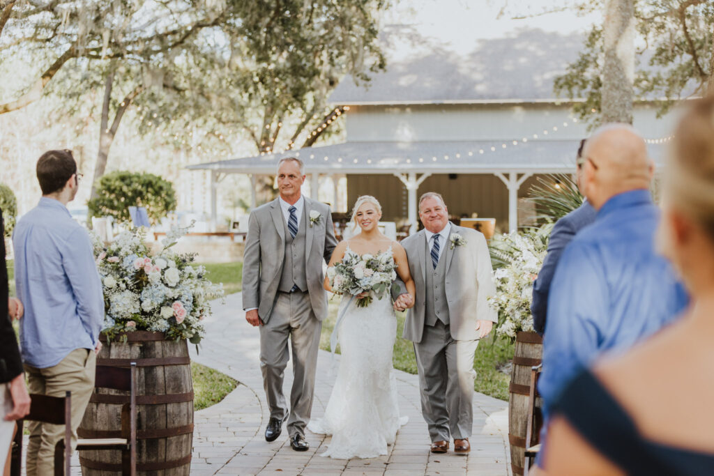 bride walking into the outdoor ceremony area of bowing oaks with her dads