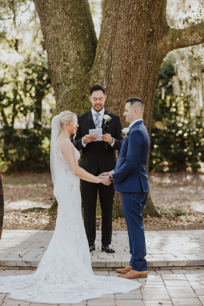 bride and groom holding hands and looking at each other during ceremony outside of bowing oaks under their giant oak tree 