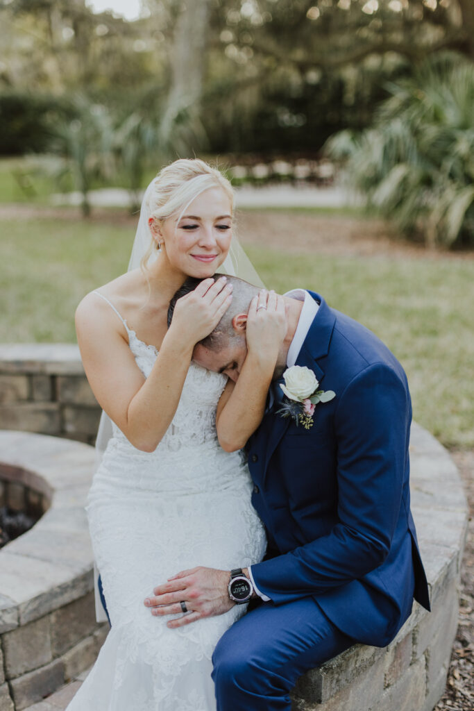 bride hugging groom's head while sitting on his lap while sitting at fire pit of bowing oaks wedding venue