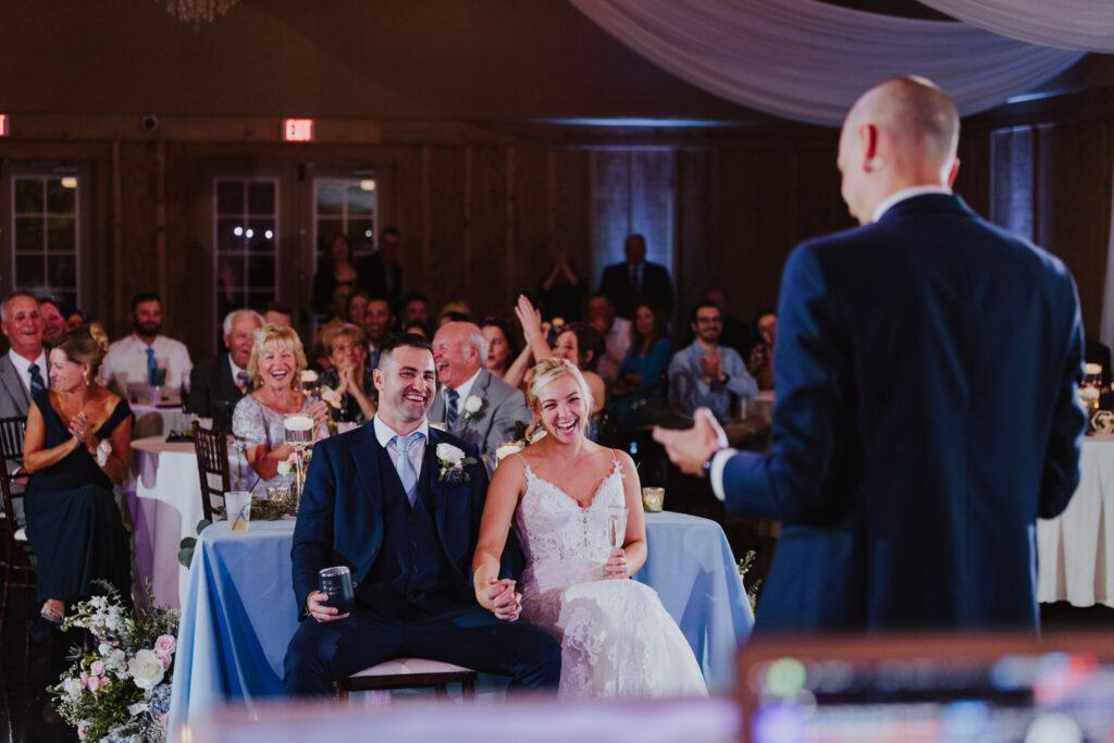 groom and bride laughing at the best man's speech with their guests behind them