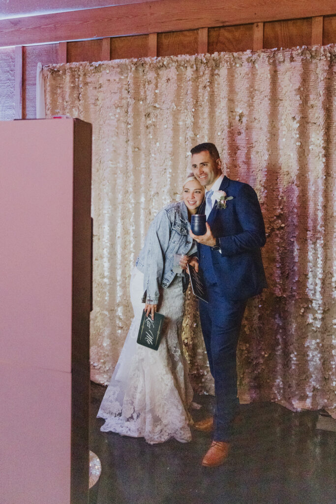 bride and groom posing in front of gold sequin backdrop of photobooth during their reception of bowing oaks