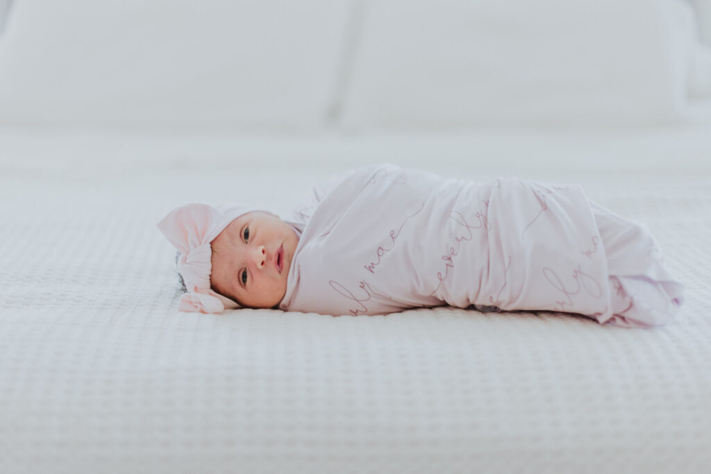 newborn baby girl wrapped in a pink blanket with a pink bow on her head