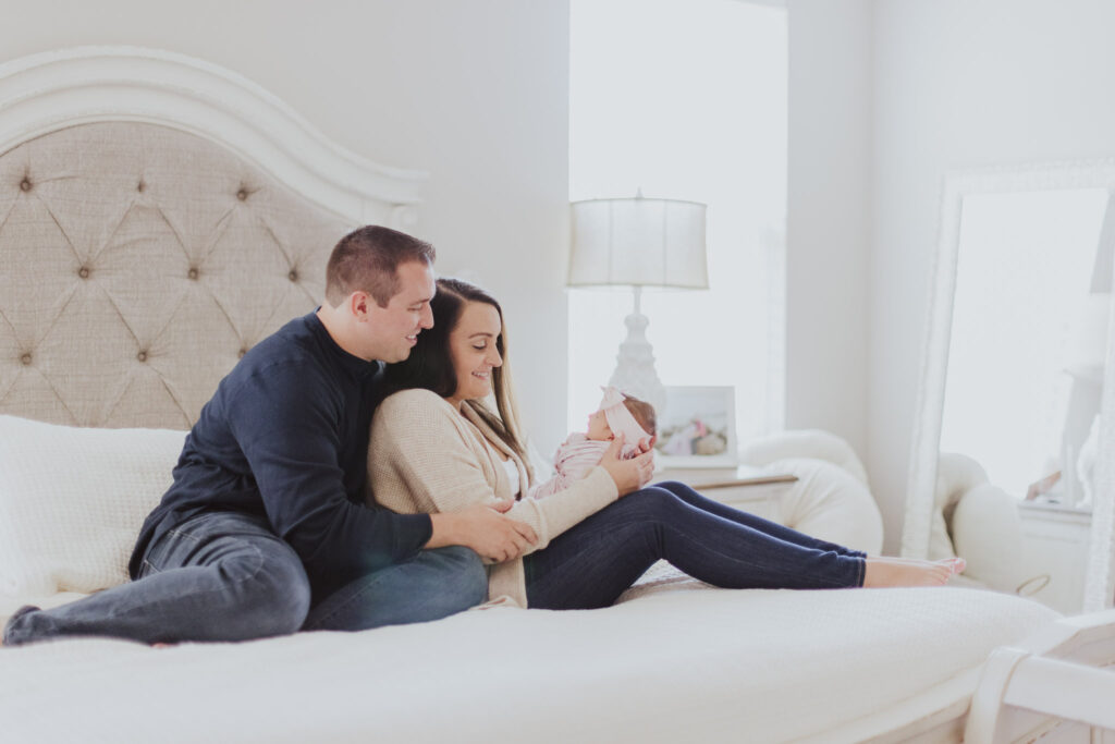 parents holding their newborn while sitting on their bed in their white bedroom