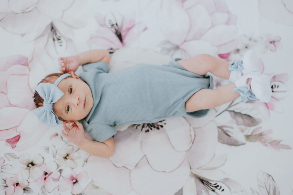 newborn baby girl in light blue outfit laying on large floral sheets