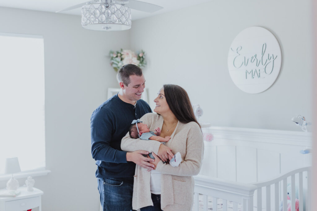parents looking at each other and holding baby while smiling and standing in her nursery