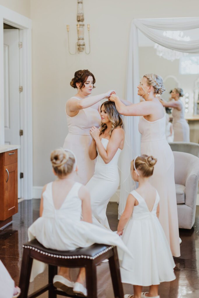 bridesmaids helping attach bride's veil into her hair in the getting ready are of the bridal suite of bowing oaks