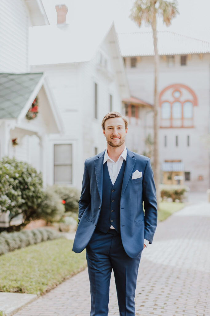 groom wearing navy suit staning on st. augustine palm row 