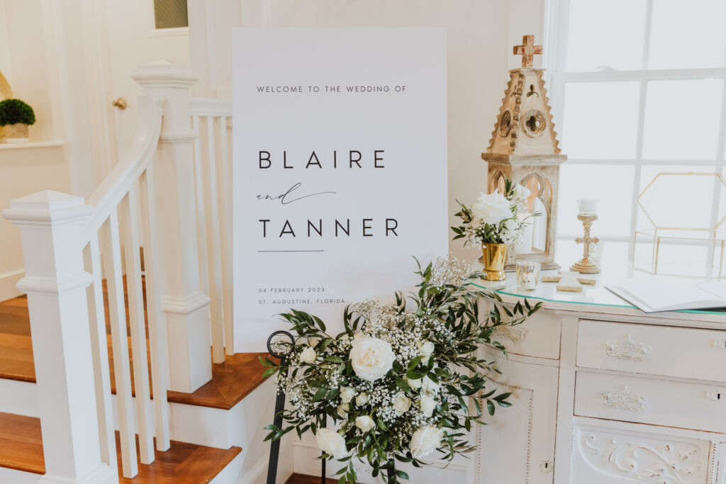 welcome sign decorated with white florals and greenery at entry of white room villa blanca ceremony space