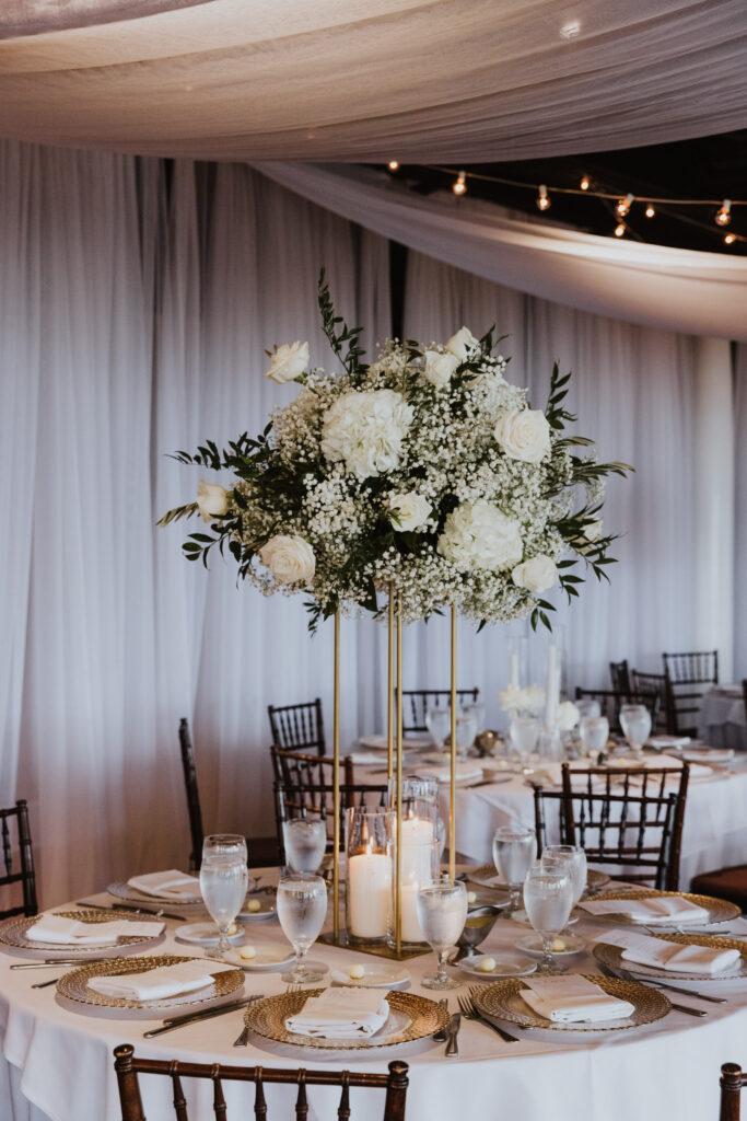 tall centerpiece with white florals and greenery and white candles and gold chargers