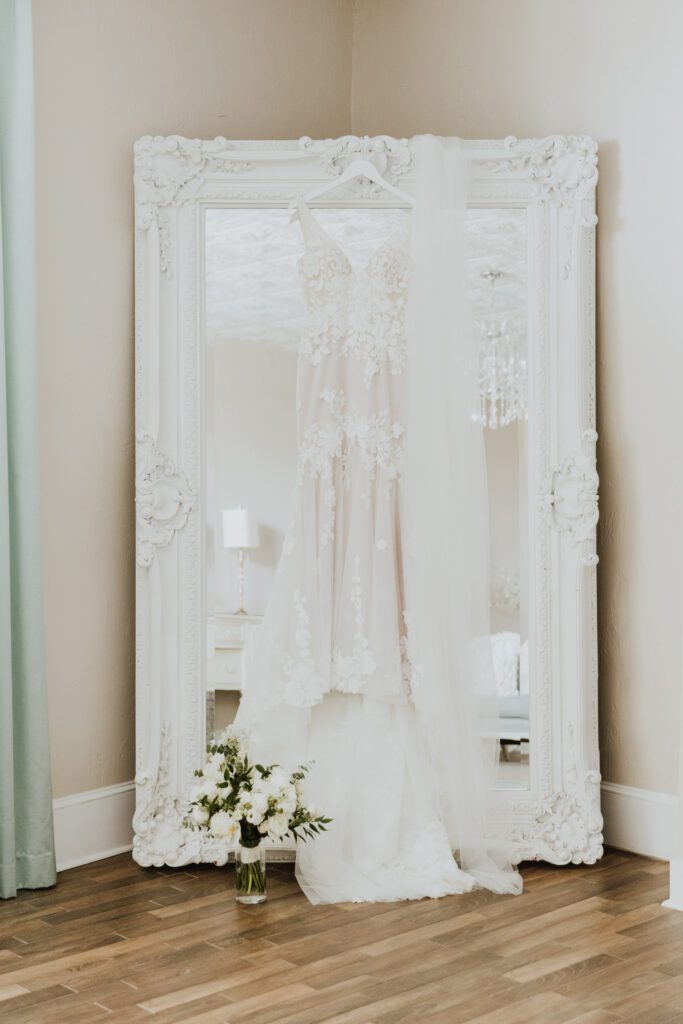 bridal gown hanging on the full length mirror of the white room grand ballroom bridal suite with bridal bouquet on floor next to it
