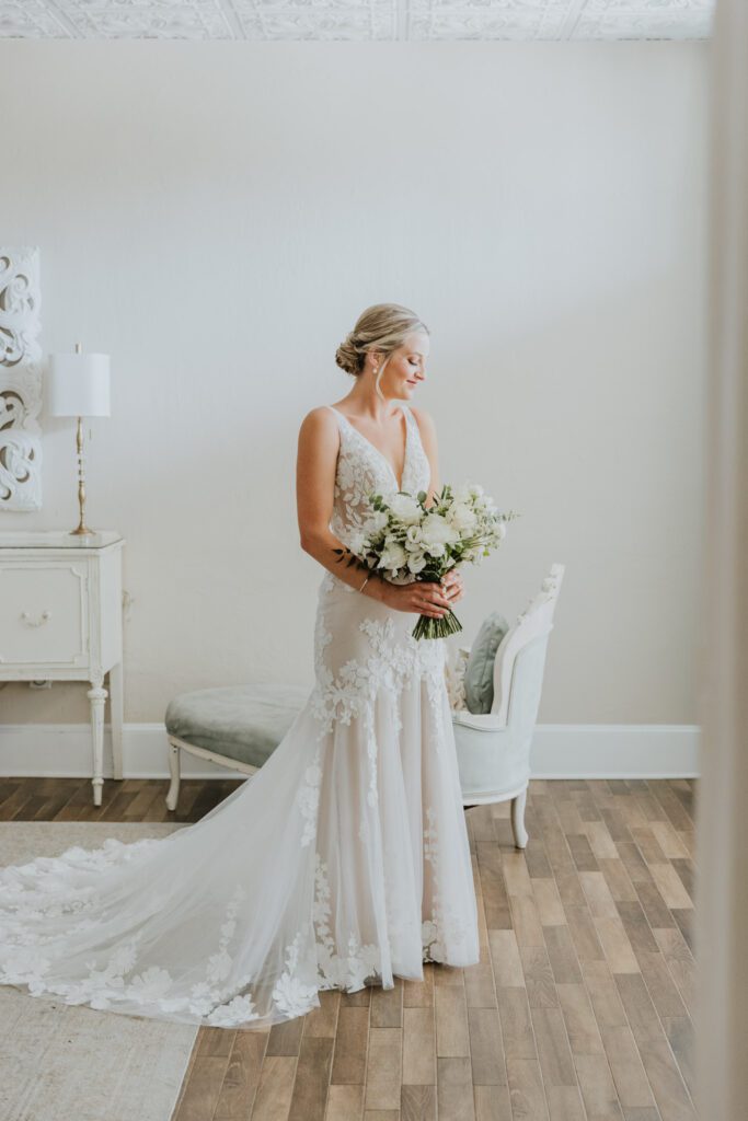 bride standing in white room bridal suite holding bouquet during bridal portrait on wedding day