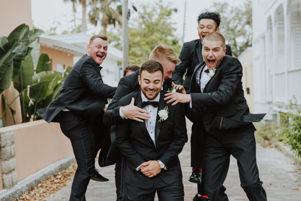 groomsmen jumping on back of groom during group photos