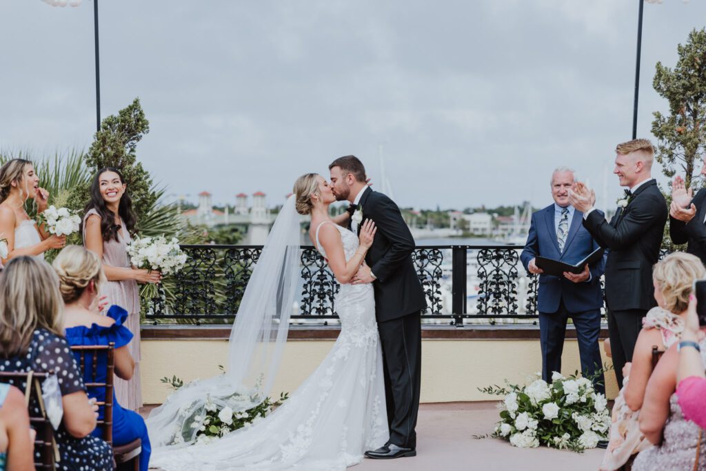 bride and groom sharing first kiss as husband and wife during ceremony on white room rooftop