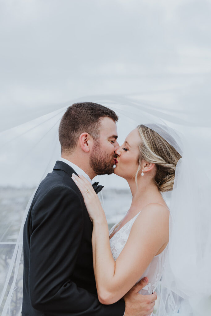 groom and bride kissing with veil hanging over heads