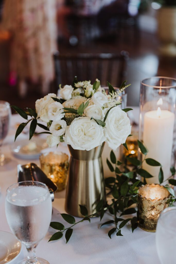 white floral centerpiece at wedding with gold vase and candles