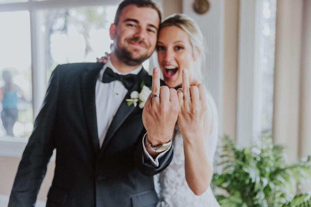 groom and bride holding up their ring fingers showing their wedding bands 
