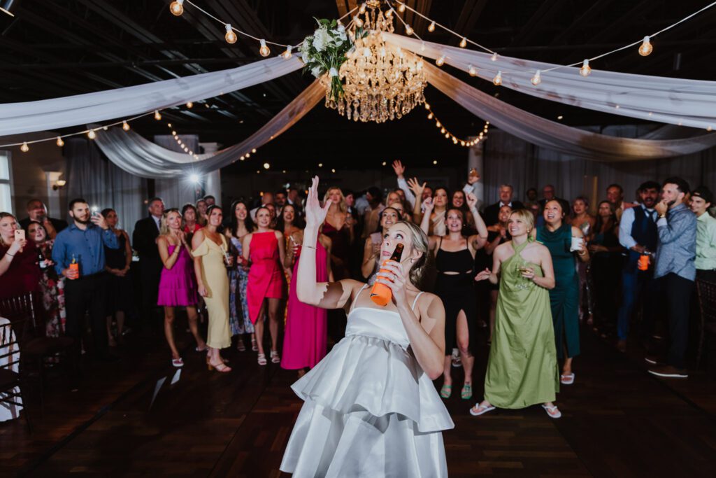 bride throwing bouquet in the air during reception on the dance floor at white room wedding
