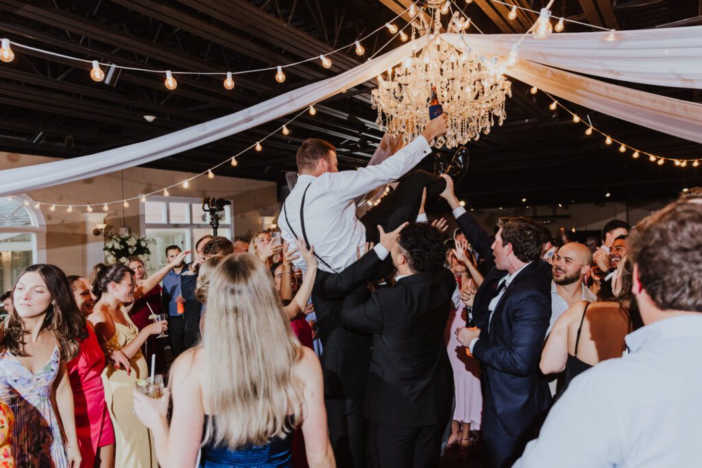 groom being lifted in the air on the dance floor of the white room grand ballroom reception